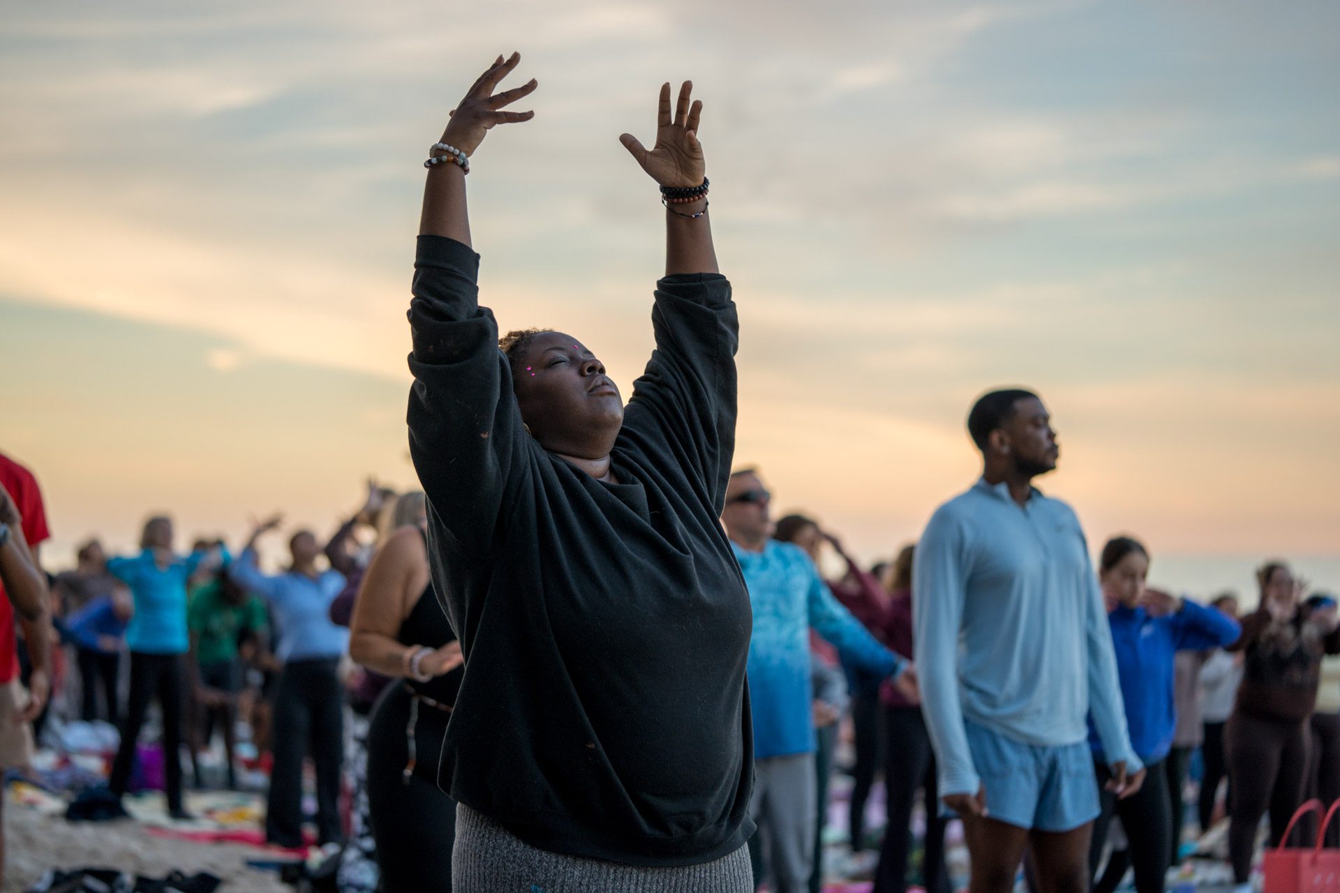 Participant raising both arms toward the sunset sky at Full Moon Beach Yoga, Atwater Beach Milwaukee